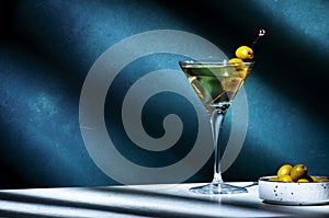 Vodka martini with olives, alcoholic cocktail drink with vodka and vermouth, dark green background, bright hard light and shadow