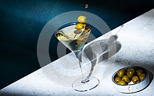 Vodka martini with olives, alcoholic cocktail drink with vodka and vermout, dark green background, bright hard light and shadow