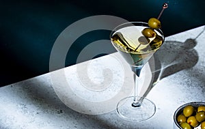 Vodka martini with olives, alcoholic cocktail drink with vodka and vermout, dark green background, bright hard light and shadow