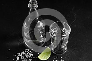 Vodka in shot glass and mini bottle on black background with a blank space for a text