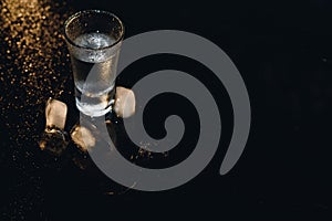 Vodka in shot glasses on black background, iced strong drink in misted glass.