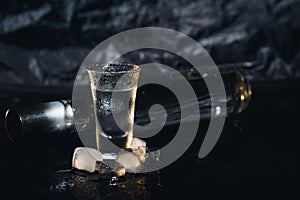 Vodka in shot glasses on black background, iced strong drink in misted glass.