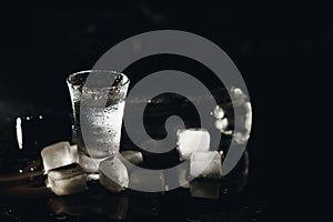 Vodka in shot glasses on black background, iced strong drink in misted glass.