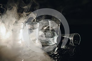 Vodka in shot glasses on black background, iced strong drink in misted glass.