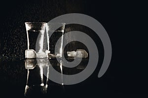 Vodka in shot glasses on black background, iced strong drink in misted glass.