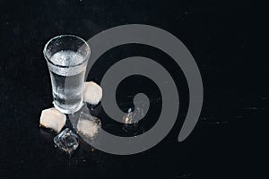 Vodka in shot glasses on black background, iced strong drink in misted glass.