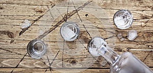 Vodka in shot glasses pouring out of the bottle on wooden background, iced strong drink in misted glass. Top view