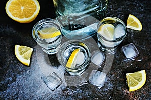 Vodka. Shots, glasses with vodka and lemon with ice .Dark stone background.