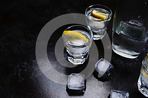 Vodka. Shots, glasses with vodka and lemon with ice .Dark stone background.