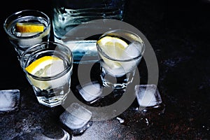 Vodka. Shots, glasses with vodka and lemon with ice .Dark stone background.