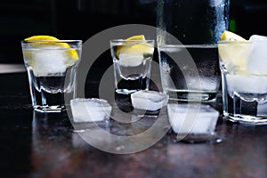 Vodka. Shots, glasses with vodka and lemon with ice .Dark stone background.