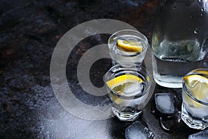 Vodka. Shots, glasses with vodka and lemon with ice .Dark stone background.