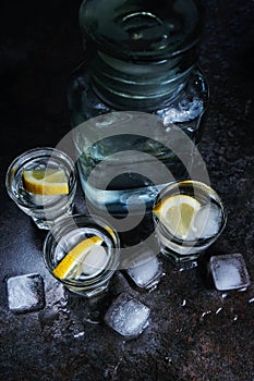 Vodka. Shots, glasses with vodka and lemon with ice .Dark stone background. Vertical image.