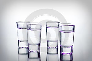 Vodka shots lighted with purple light filled with alcohol on glass bar table