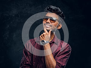 Vogue, fashion, style. Cheerful young Indian guy wearing a stylish shirt and sunglasses posing with hand on chin.