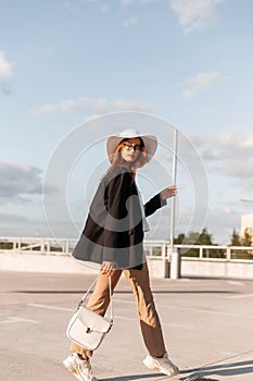 Vogue woman in fashion black blazer and stylish pants in elegant hat in shoe with bag travel outdoors in sunny day. Trendy girt in