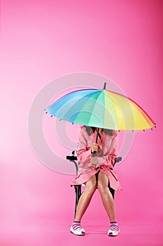 Vogue. Woman in Pink Coat sitting with Colorful Umbrella