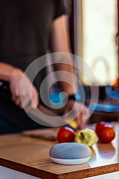 voice controlled smart speaker in a interior kitchen. Man cutting vegetables in background.