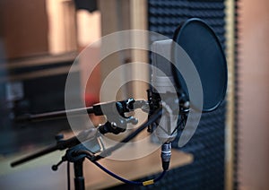 Voice microphone with shock mount and pop filter on professional tripod in audio recording studio.