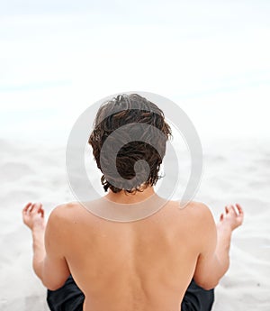 The voice of the sea speaks to his soul. Young handsome man sitting on the beach meditating.