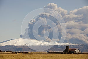 Volcanic eruption beneath the EyjafjallajÃ¶kull glacier with a farm in the foreground.