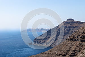 Volcanic high cliffs reaching into the ocean with a blurred view on Oia, Fira, Santorini, Greece