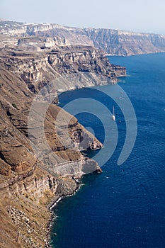 Volcanic high cliffs reaching into the ocean with a sailboat, Fira, Santorini, Greece