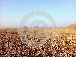 Volcanic landscape. Desert area with stones, rocks and sandstone and silhouette of volcano slopes on the horizon under blue sky.