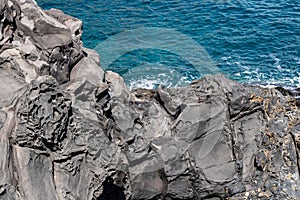 Volcanic rock formations texture with the blue sea on the background - Image