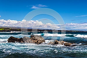 Volcanic rock, ocean and surf; Punaluu Black Sand Beach in Hawaii. Clouds and sky in background; shoreline in distance.