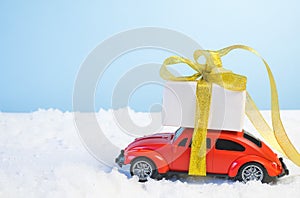 Volgograd, Russia - October 15, 2021: Small red retro toy car with a gift box with a gold ribbon and a Christmas tree on