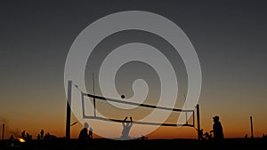 Volleyball net silhouette on beach court at sunset, players on California coast.