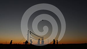 Volleyball net silhouette on beach court at sunset, players on California coast.