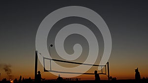 Volleyball net silhouette on beach court at sunset, players on California coast.