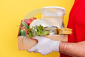 A volunteer brings a box of food. Fresh vegetables and groceries in a cardboard box on a yellow background, donation.