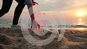 Volunteer cleaning the beach of plastic garbage. Woman picking up trash from the sand at the sea shore. Plastic pollution,