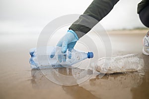 A volunteer collects used plastic bottles on the ocean shore. Environmental and social issues. Poisoning of the environment -