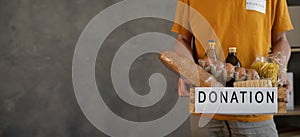 Volunteer with donation box with food, close up. A man holding a donations box of different products on grey background