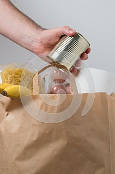 Volunteer with donation box with foodstuffs. Male hands hold a set of food products in a paper bag