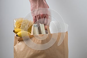 Volunteer with donation box with foodstuffs. Male hands hold a set of food products in a paper bag