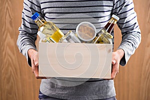 Volunteer with donation box with foodstuffs on wooden background