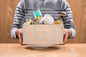 Volunteer with donation box with foodstuffs on wooden background photo