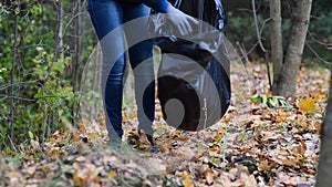 Volunteer girl collects trash in a bag, cleaning up the forest. Close up