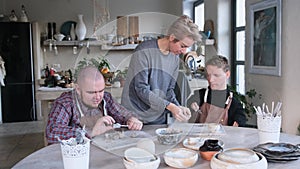 A volunteer girl conducts a clay modeling master class for men with disabilities, helping them to master pottery. Social