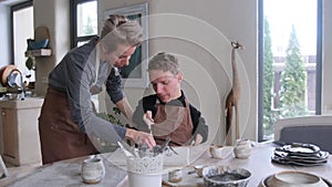 A volunteer girl conducts training for a guy with congenital physical disabilities, learns clay modeling while sitting