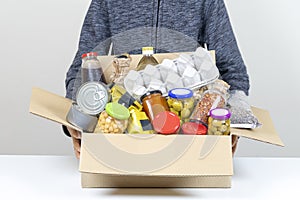 Volunteer hands holding food donations box with grocery products on white desk