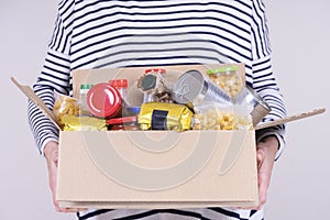 Volunteer hands holding food donations box with grocery products on white desk