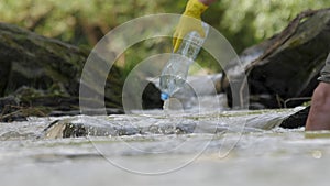 Volunteer hands picks up a plastic bottles from mountain river clean up waste water. Plastic garbage water flows river