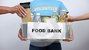 Volunteer holding food bank container, hands putting provision in box, help
