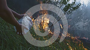 A volunteer man or boy extinguishes a wild fire. Pours water from a plastic bottle. Rain forest wildfire disaster, dry